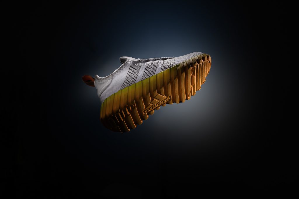 Adidas Sneaker mit strukturierter Gummisohle im Studio, dramatisch ausgeleuchtet auf schwarzem Hintergrund.