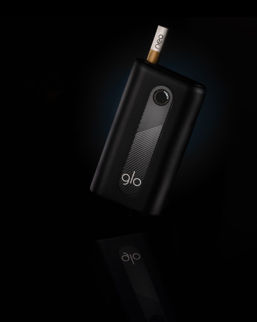 Schwarzes glo Tabakerhitzungsgerät mit eingesetzter neo-Stick – hochwertig fotografiert mit Spiegelung von einem Produktfotografen in Zürich.“