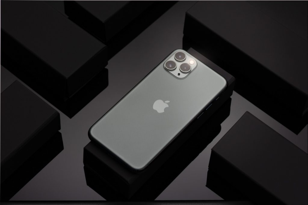 iPhone mit Dreifachkamera auf schwarzem Untergrund und eleganten Verpackungselementen – edel fotografiert von einem Produktfotografen aus Zürich.