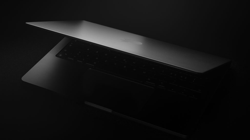 Dramatisch beleuchtetes MacBook Pro mit halb geöffnetem Displaydeckel – fotografiert in Low-Key-Ästhetik von einem Technik- und Produktfotografen aus Zürich.
