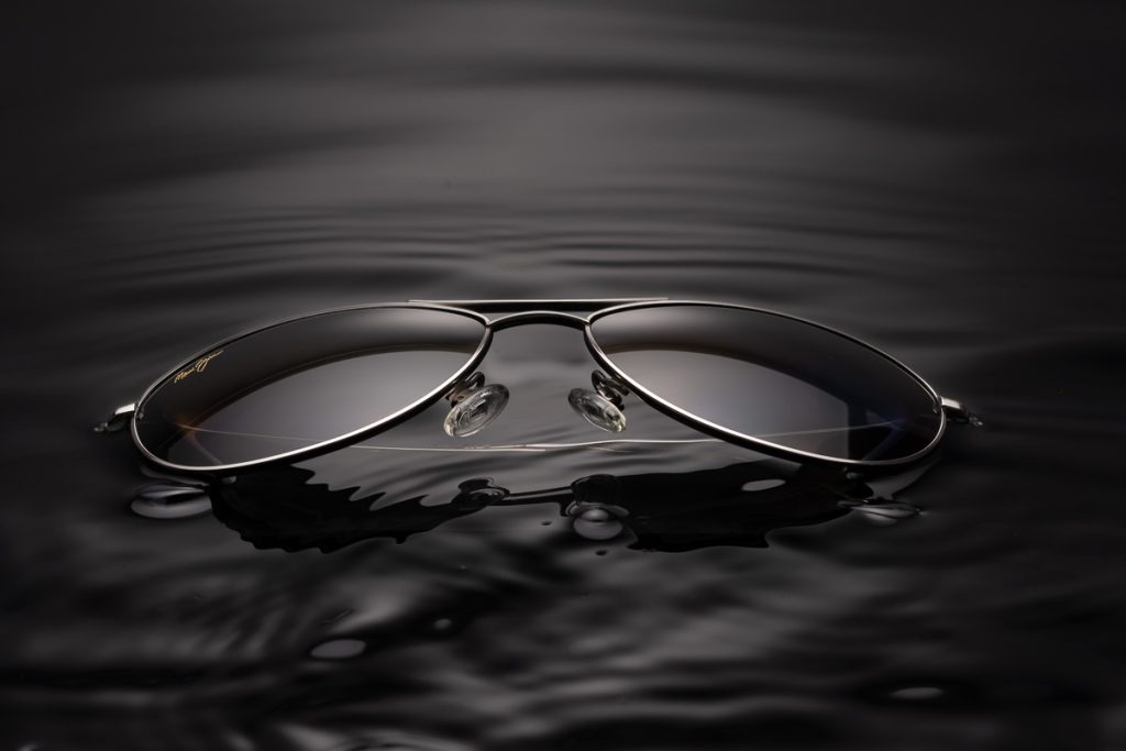 Luxuriöse Sonnenbrille mit Metallrahmen, die in dunklem Wasser schwimmt – inszeniert von einem kreativen Produktfotografen aus Zürich.